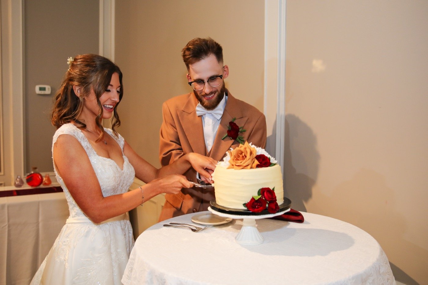 A couple cutting their Kaylee's Kitchen wedding cake topped with roses